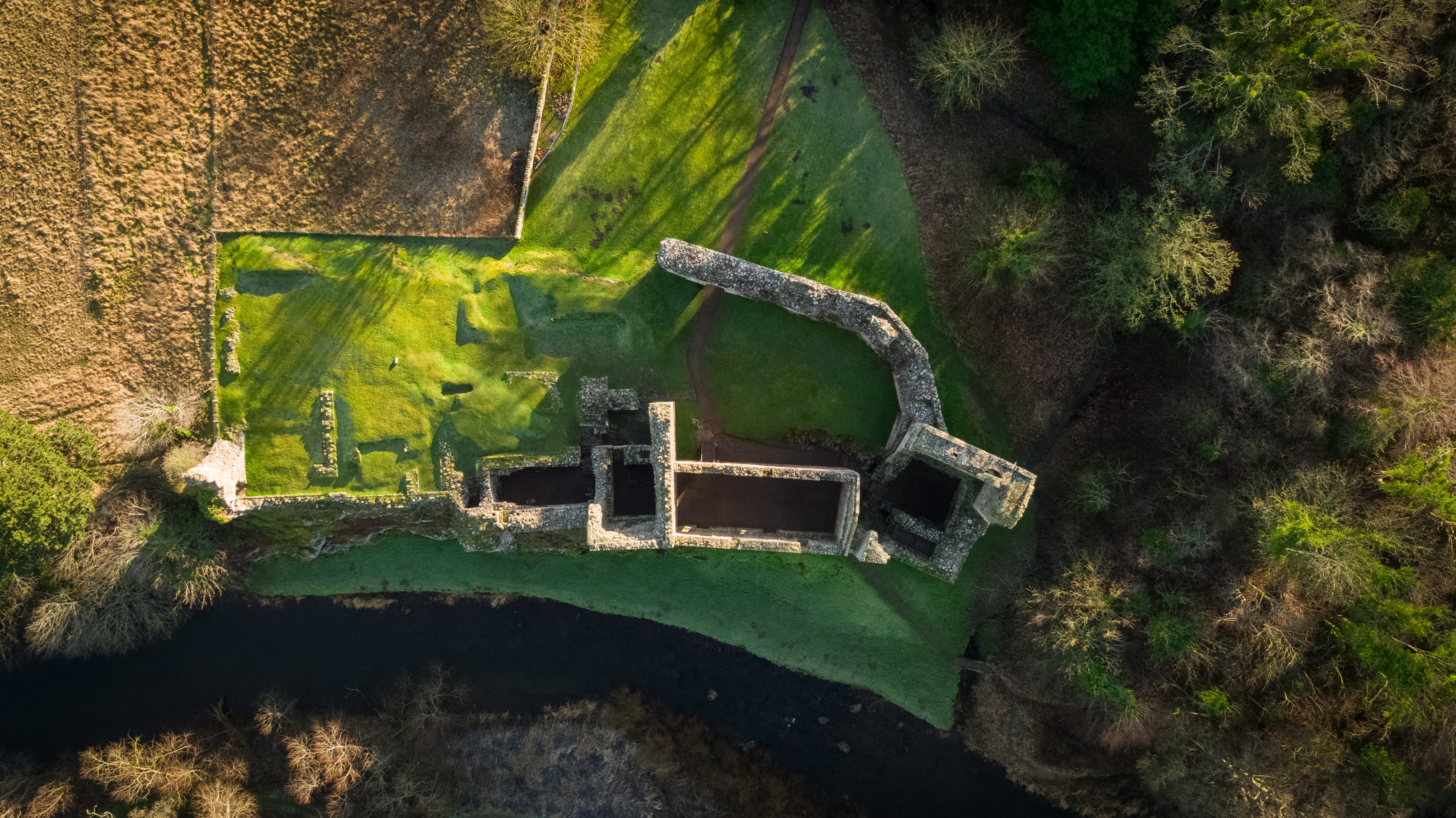 Top-down aerial image of ruins of Hailes Castle surrounded by green grass, woodland and fields. 