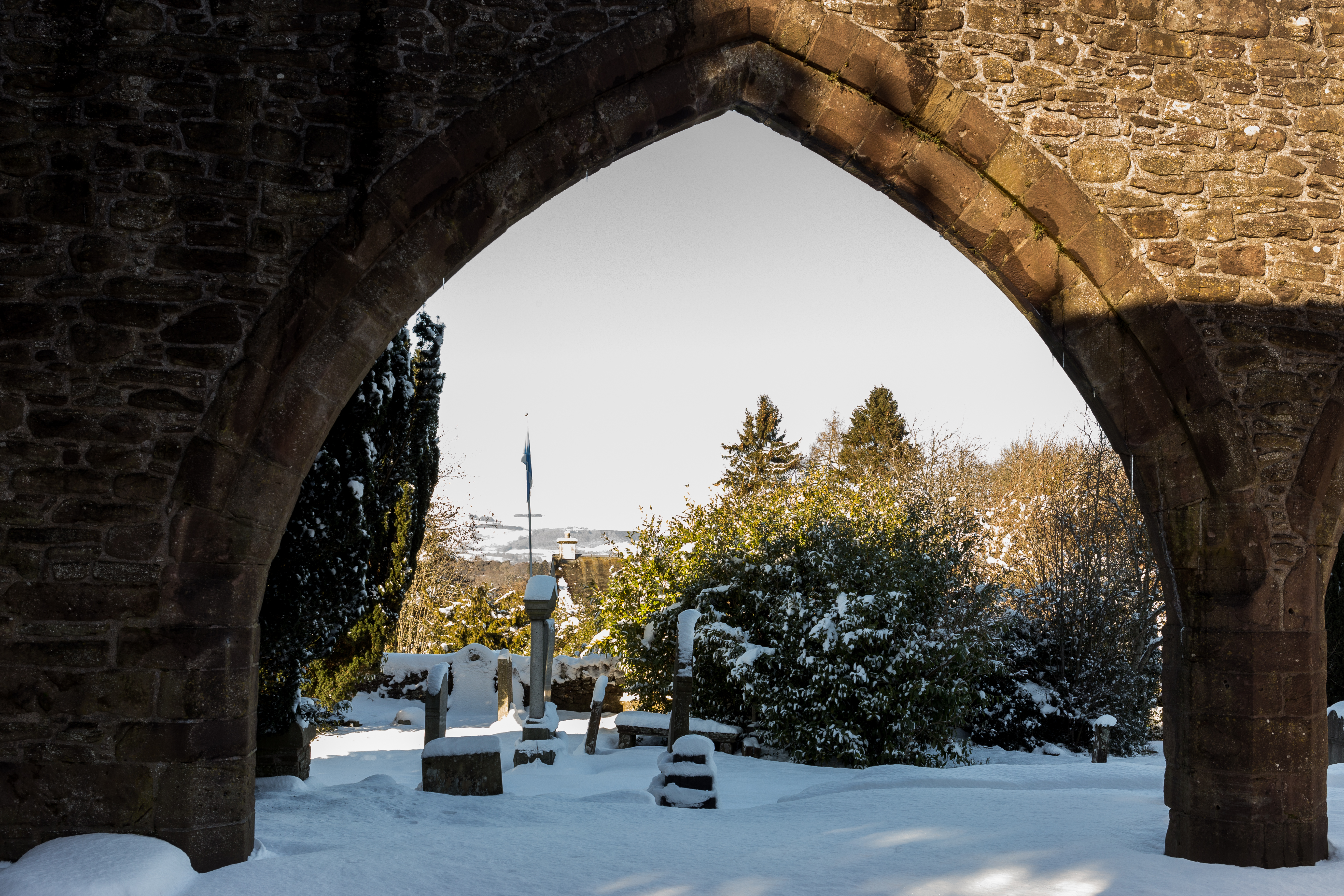 A view through a large pointed arch of the ruined church, looking out onto snow-covered gravestones and trees.