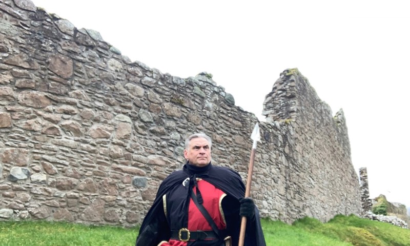 A costumed performer standing with a spear in front of a ruinous wall