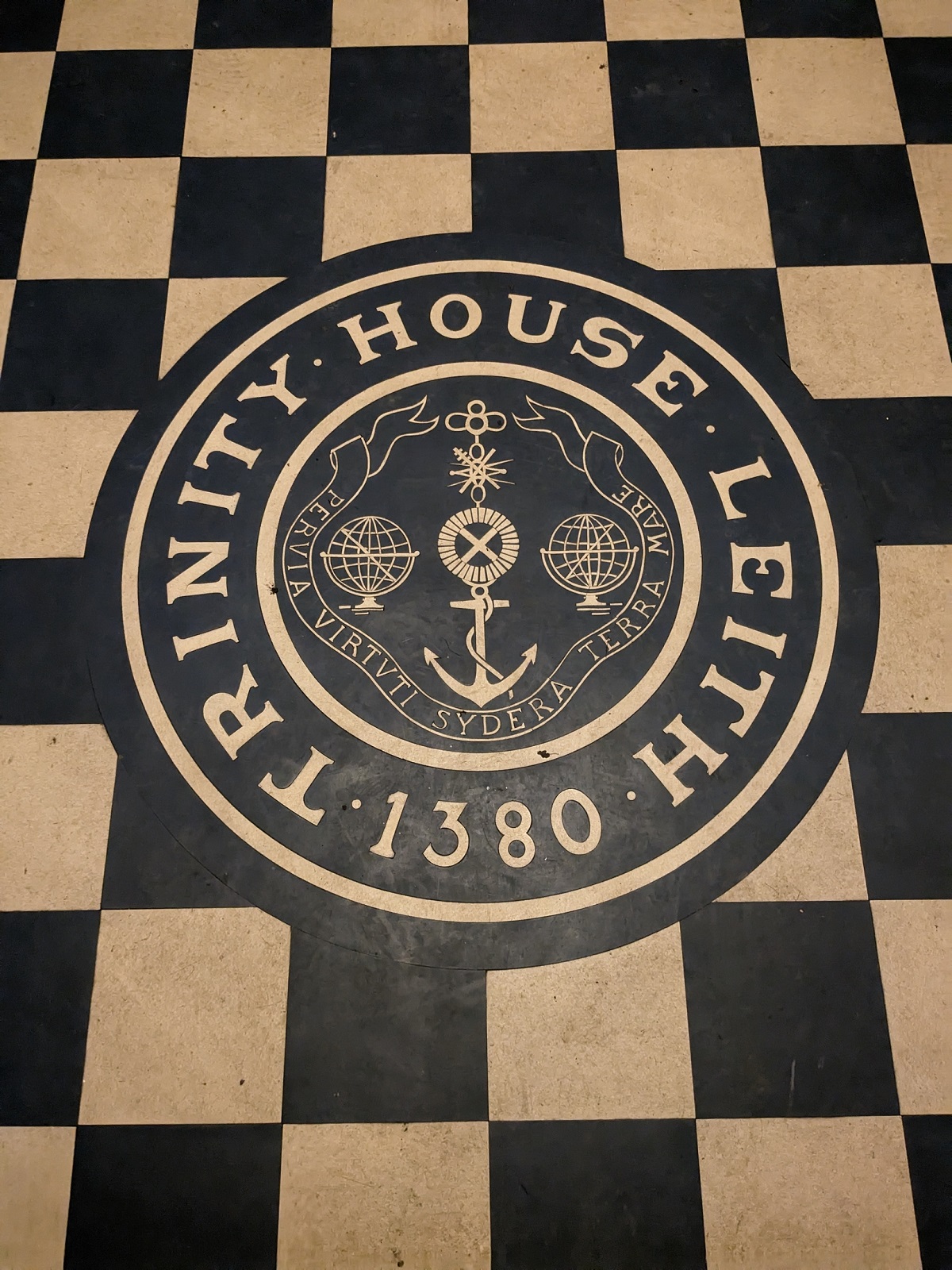 Circular Trinity House seal set into a black‑and‑cream chequered floor, featuring an anchor and maritime symbols with the date 1380.