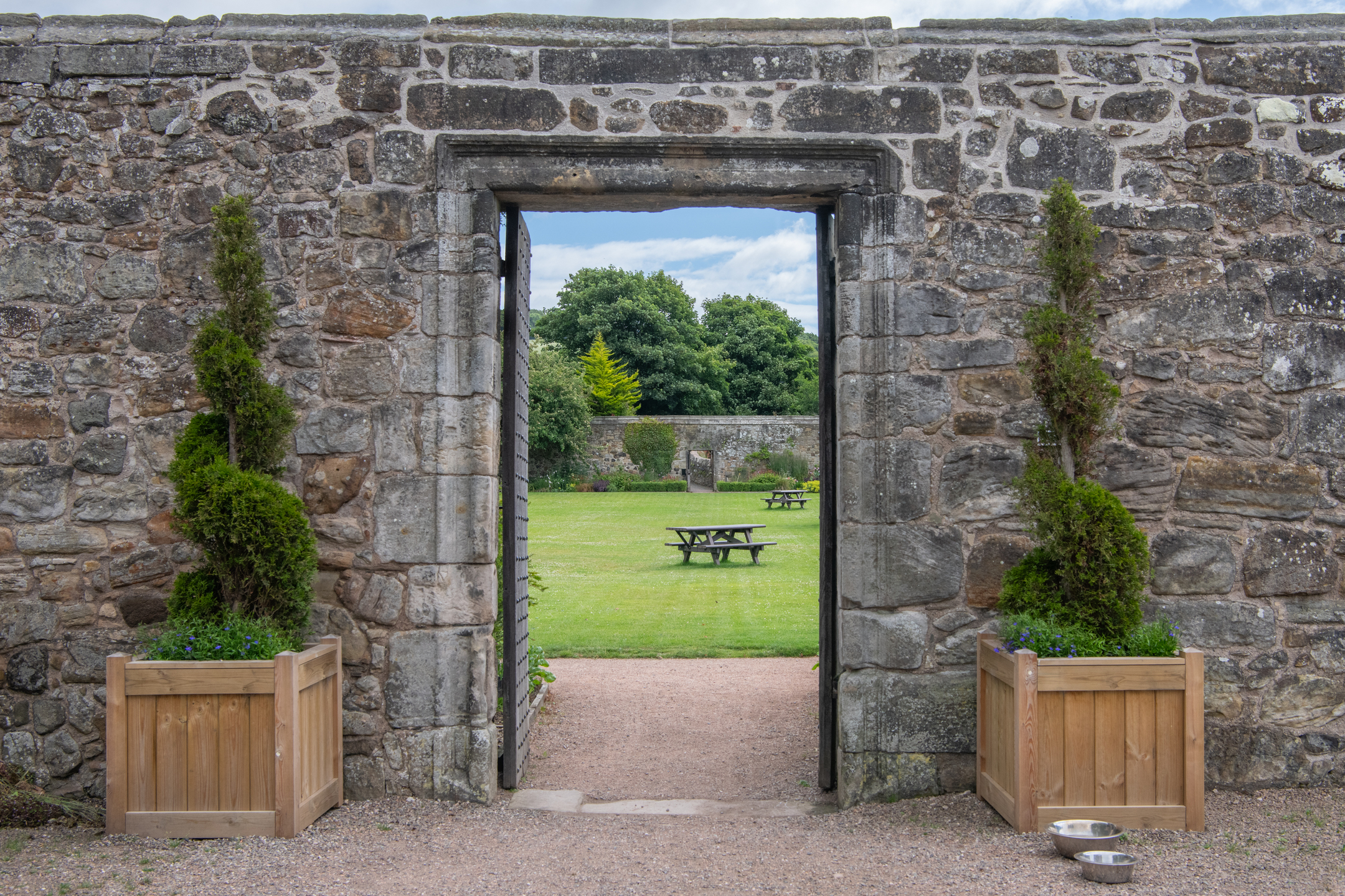 A doorway in a historic stone wall, looking onto a grassy area with picnic benches