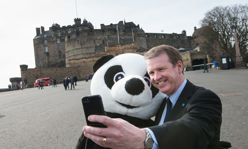 A photograph of a man taking a selfie beside a person dressed in a giant panda costume.