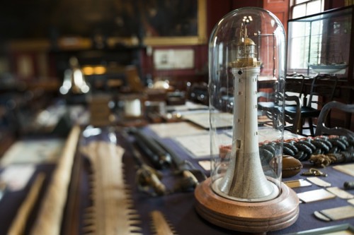 A photograph of a small model lighthouse on a table, surrounded by naval items.
