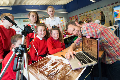 School children crowd around a laptop to be shown a display by a teacher