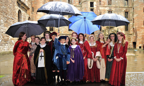 Junior Tour Guides at Linlithgow Palace in costumes under umbrellas