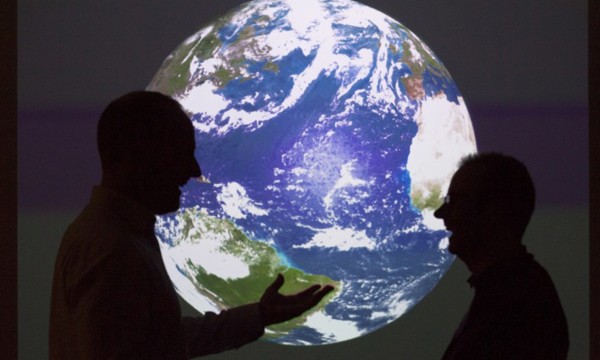 two figures face each other in conversation, silhouetted against a brightly lit backdrop of planet earth viewed from space