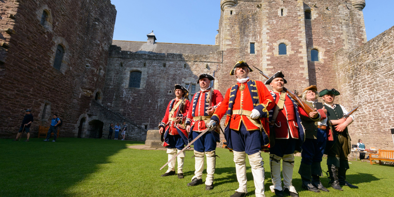 A group of 6 men in re-enactment clothing at a castle, with bayonets