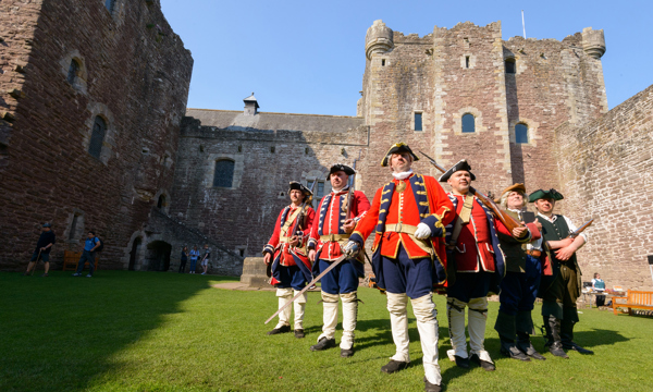 A group of 6 men in re-enactment clothing at a castle, with bayonets