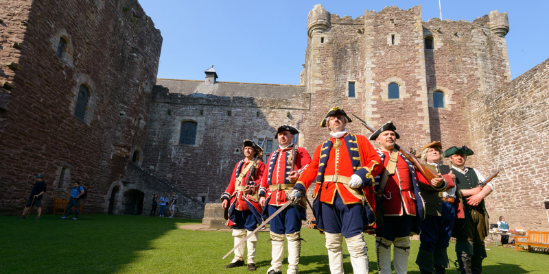 A group of 6 men in re-enactment clothing at a castle, with bayonets