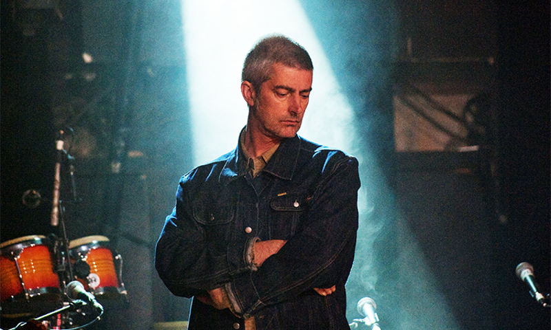 Frontman of Shooglenifty on stage with backlighting