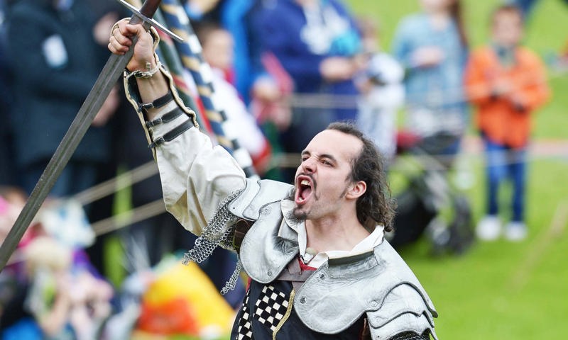 A jouster at Linlithgow Palace celebrating on horse back, cheering with the crowd, clutching a sword by the blade