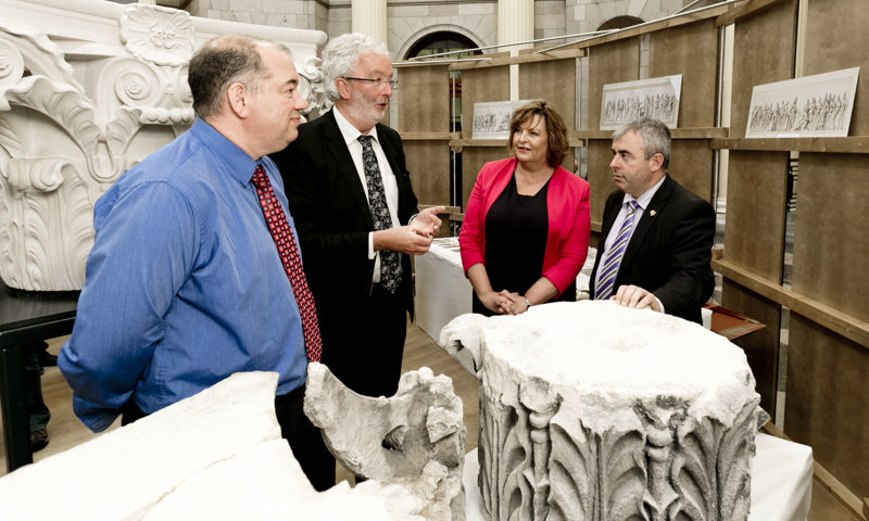 four people stand in a line discussing a carved column