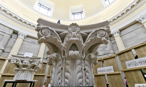 section of a white story column with a leave motif carved into it, with domed roof above 