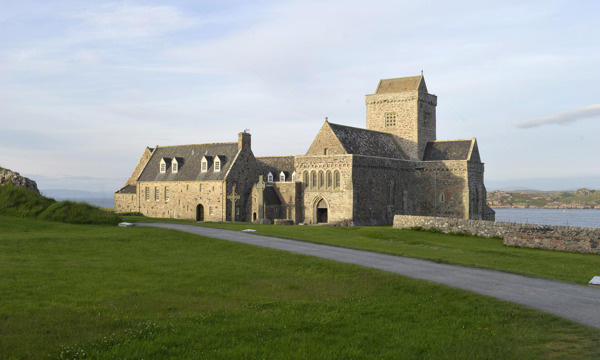 abbey building with grass in front and sea behind