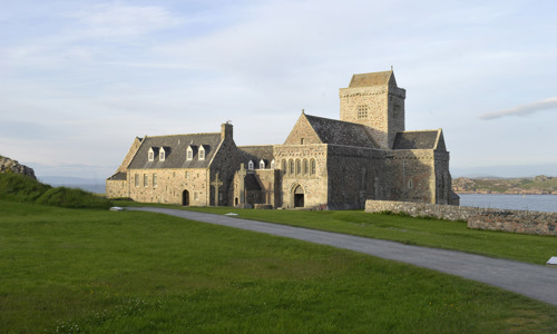 abbey building with grass in front and sea behind