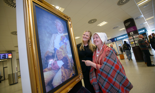 two smiling women look at a portrait of a prince in a gold frame