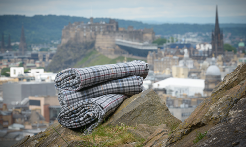 A photograph of a set of tweet blankets on top of some rocks with a castle and city in the distance