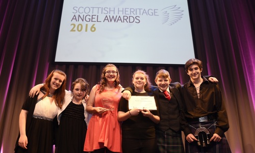 A photograph of six young people dressed in formal attire holding an award and certificate, smiling at the photographer.