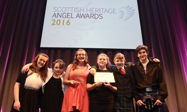 A photograph of six young people dressed in formal attire holding an award and certificate, smiling at the photographer.