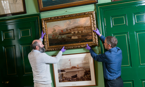 Two curators hanging a painting in a frame at a gallery