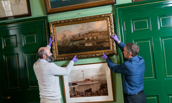 Two curators hanging a painting in a frame at a gallery