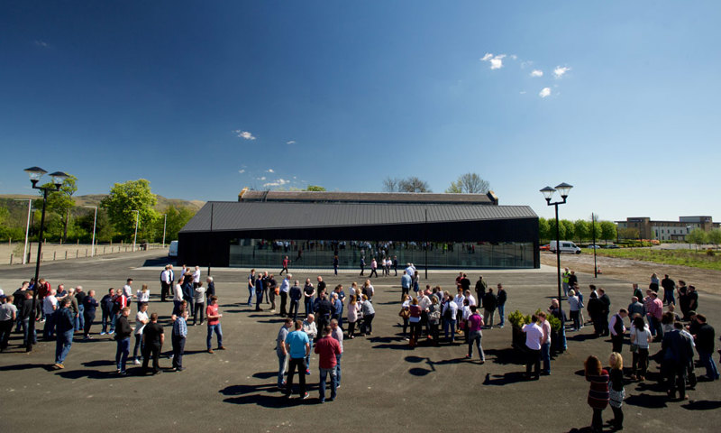 Photograph of groups of people congregating outside a modern building on a sunny day