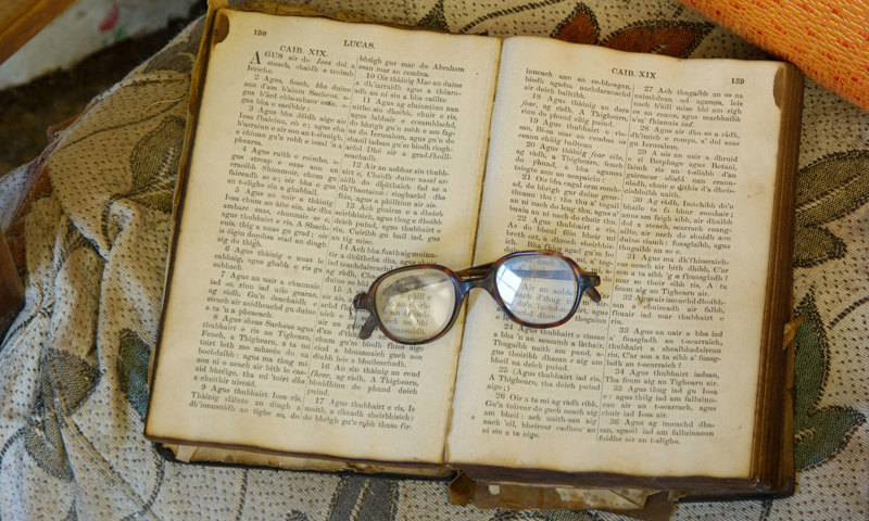 A photograph of a book written in Gaelic lying open with a pair of glasses sitting on top