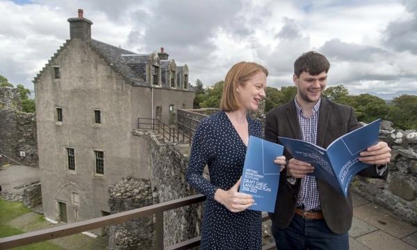 a woman and a man hold copies of a document in front of a castle 