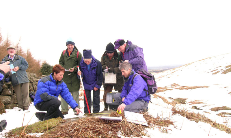Photograph of a group of volunteers on a snowy hill learning how to record rock art 