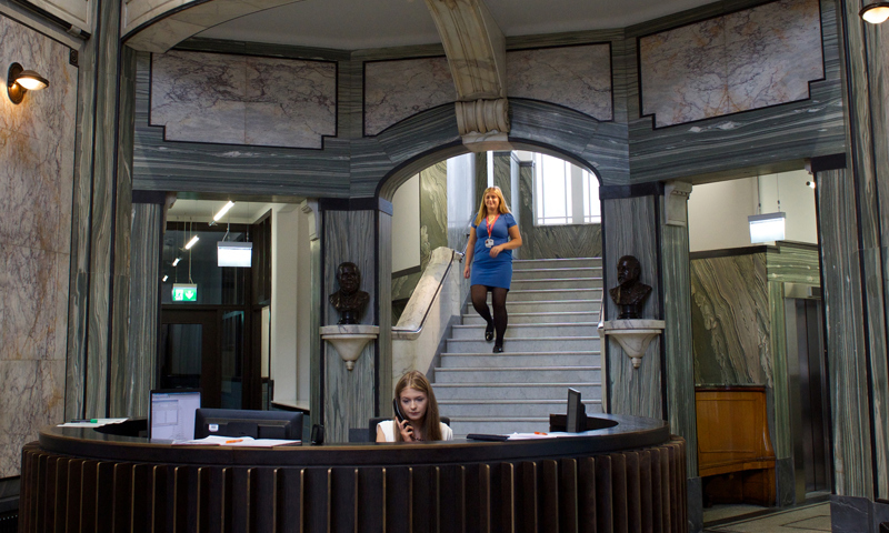 Reception at Russell Institute with receptionist at her desk, and a woman walking down some stairs in the background