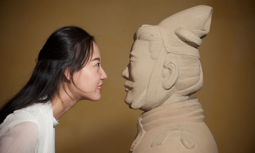 A woman holding her face up close to the face of a Chinese statue