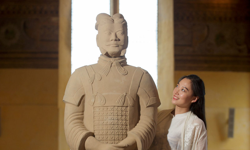 A woman standing behind and to the side of a Chinese statue