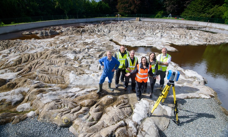team of six people stand on a concrete map with a laser camera used in survey work, smiling at the camera