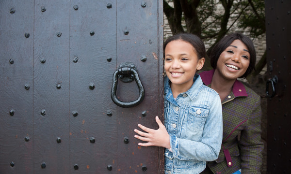 two visitors peer out from behind a historic wooden door