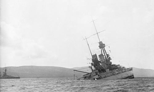 A black and white photograph of a metal ship sinking in choppy water