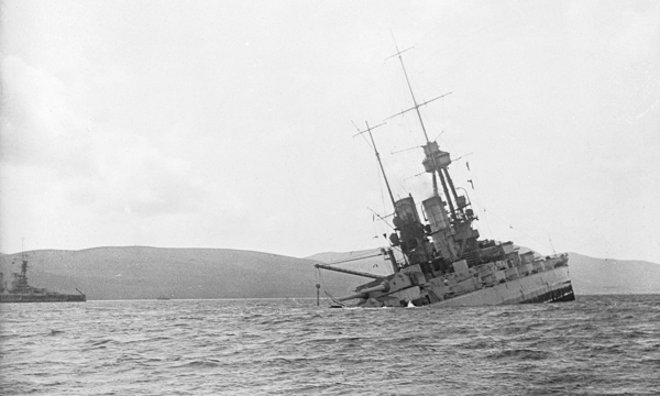 A black and white photograph of a metal ship sinking in choppy water