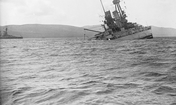 A black and white photograph of a metal ship sinking in choppy water