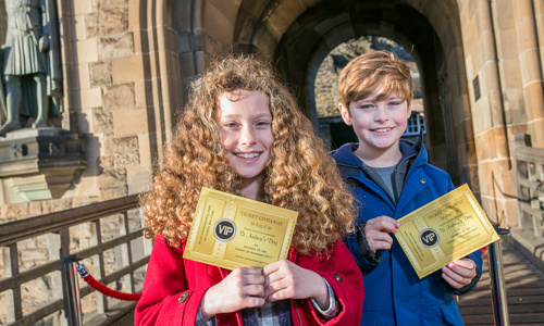 a girl and a boy holding tickets stand outside a historic arch smiling at the camera