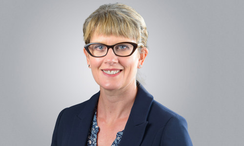 A woman with short blonde hair and wearing glasses smiling at the camera.