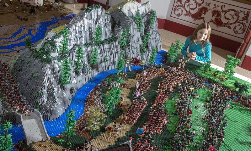 small girl looks at lego model of mountain range with soldiers, trees and river in the scene