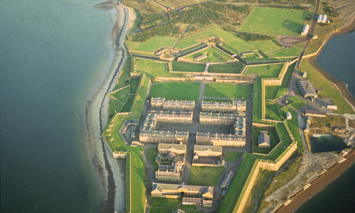 aerial image looking down at coastline with building complex and woodland behind it