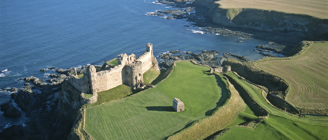 aerial image showing ruined castle on curved coastline with sea behind it