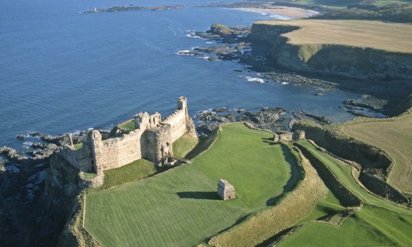 aerial image showing ruined castle on curved coastline with sea behind it