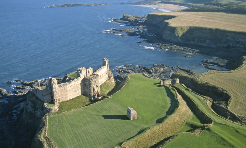 aerial image showing ruined castle on curved coastline with sea behind it