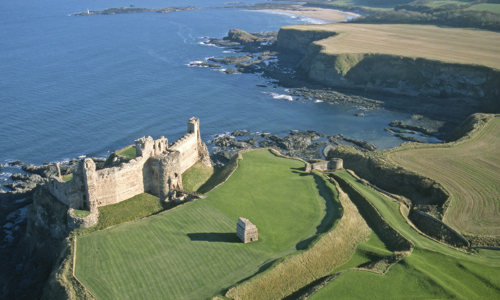 aerial image showing ruined castle on curved coastline with sea behind it