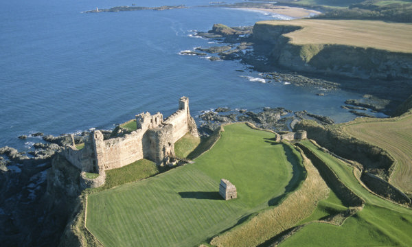 aerial image showing ruined castle on curved coastline with sea behind it