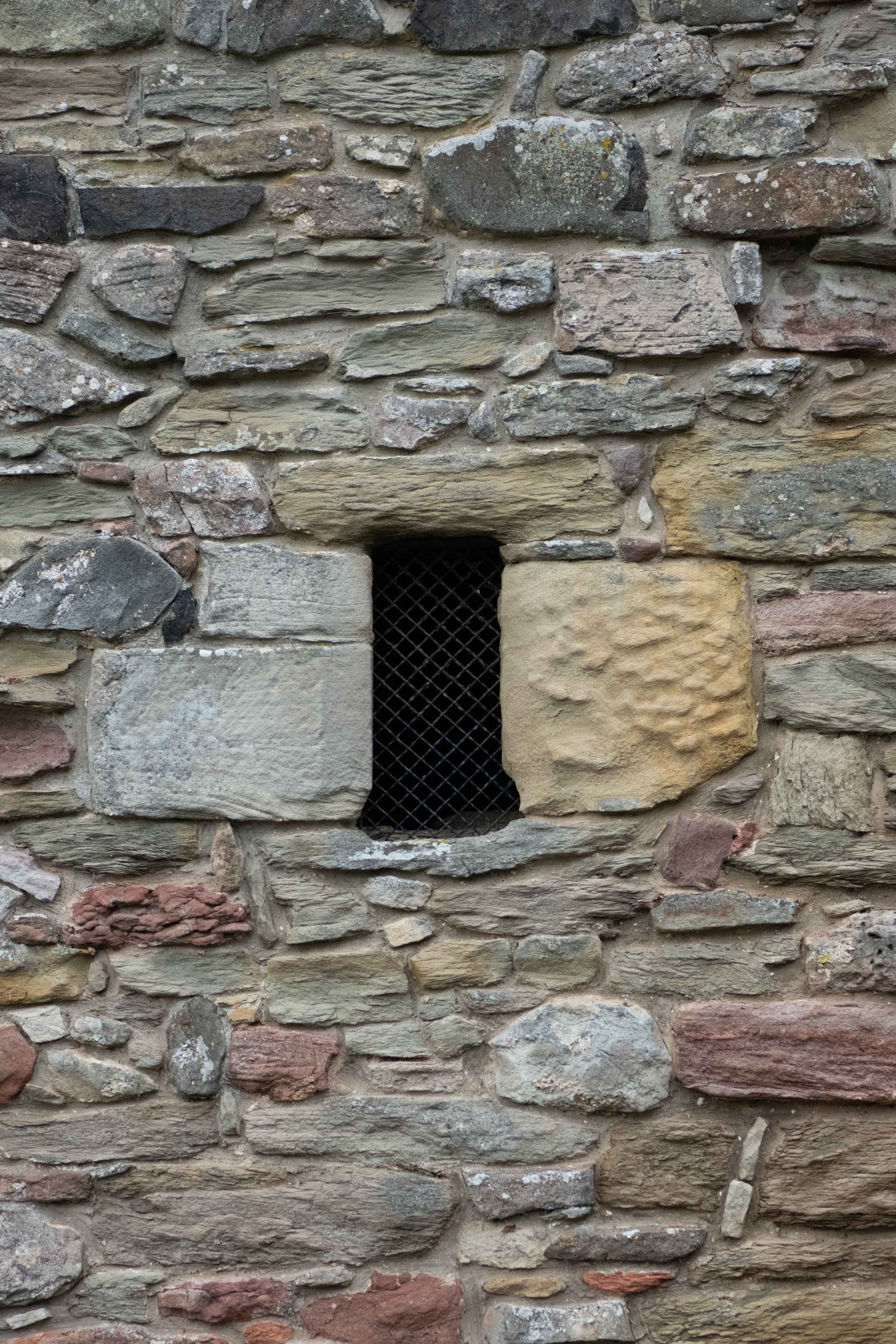 A small hole covered with a metal grate, built into the side of a sandstone wall
