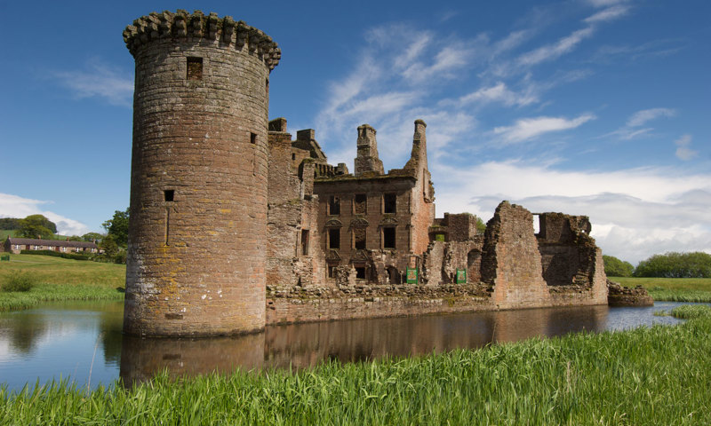 A photograph of a castle surrounded by water, with a blue sky and green grass.