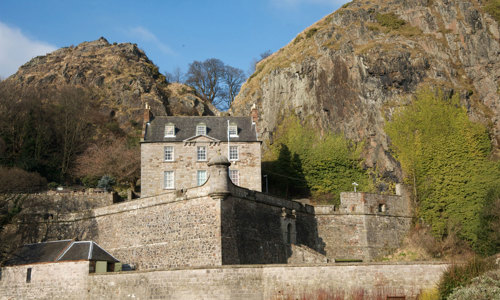 A photograph of a castle with two hills and a bright blue sky in the background.