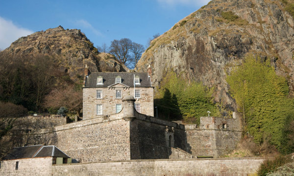 A photograph of a castle with two hills and a bright blue sky in the background.